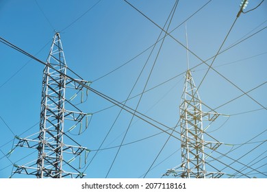 Overhead power line. High-voltage power pylons low angle view. Electricity transmission line against bright blue sky.