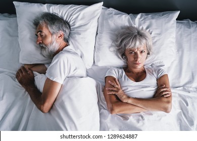 Overhead Of Senior Couple In The Bed. Pretty Aged Woman Is Angy With Her Sleeping Husband.