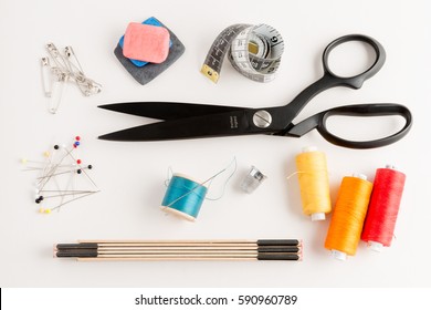 Overhead Shot Of Basic Sewing Tools Including Fabric Shears, Thimble, Pins, Tailor's Chalk, Spools Of Thread, And A Folding Ruler On A White Background