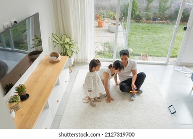 Overhead Shot Of A Beautiful Asian Family Sitting On The Living Room Carpet Playing A Game. 