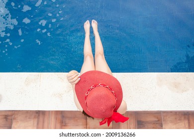 Overhead Shot Of A Beautiful Young Girl In Red Hat Sitting On The Edge Of The Pool.