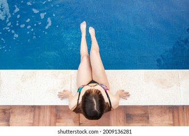 Overhead Shot Of A Beautiful Young Girl Sitting On The Edge Of The Pool.