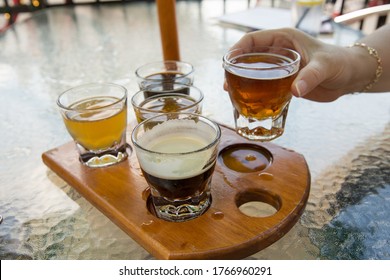 Overhead Shot Of A Beer Flight On A Wooden Board With Womans Hand Reaching For A Glass.