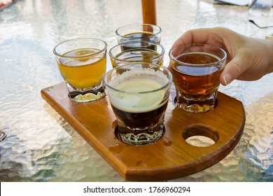 Overhead Shot Of A Beer Flight On A Wooden Board With Womans Hand Reaching For A Glass.