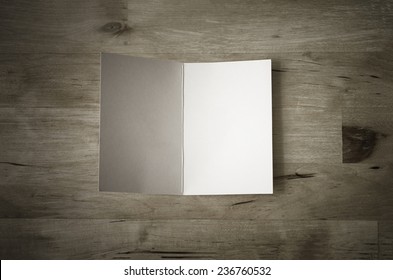 Overhead Shot Of A Blank Greeting Card, Lying Face Upwards And Opened On A Wooden Planked Table.  Low Saturation And Vignetted Vintage Style.