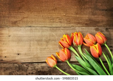 Overhead shot a bouquet of orange and yellow tulips over a rustic wood table top. Flat lay overhead view style.