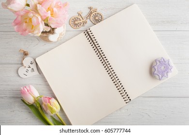 Overhead shot a bouquet of pink tulips and paperweight over white wood table top with an open journal. Flat lay top view style.