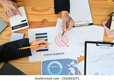 Overhead Shot Of A Business Meeting Table With Businesspeople's Hands Working On The Business Report Paperwork.