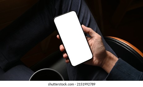 Overhead shot, Businessman using his cellphone, reading an informations or email on the phone screen at his desk. Phone white screen mockup.