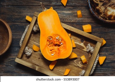Overhead shot of butternut squash with seeds on rustic wooden tray. Pumpkin pieces, harvest, fall. Dark brown background. Cooking in autumn. Healthy food.