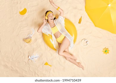 Overhead shot of cheerful young Asian woman enjoys listening favorite music wears wireless headphones on ears dressed in bikini poses at sandy beach has lazy day. Unforgettable vacation concept - Powered by Shutterstock