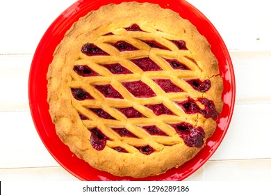 Overhead Shot Of A Cheery Pie On A Red Plate With Lattice Pastry Strips On A White Wood Table.