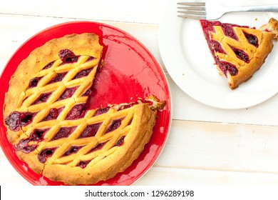 Overhead Shot Of A Cheery Pie On Red Plate With Lattice Pastry Strips On A White Wooden Table.