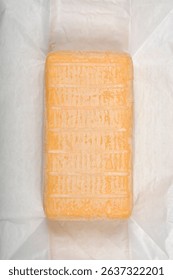Overhead shot displays a rectangular block of Limburger cheese, revealing its distinct yellowish, textured rind, nestled on a white wrinkled surface