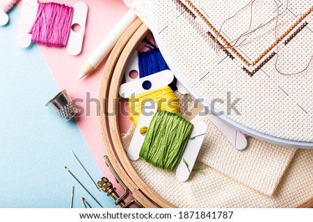 Overhead shot of embroidery set fot cross stitching. White fabric, embroidery hoop, colorful threads, scissors and needls. On pink blue background. Hobbies concept with copy space.