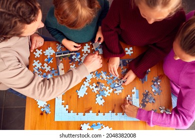 Overhead Shot Of Family Sitting Around Table At Home Doing Jigsaw Puzzle Together