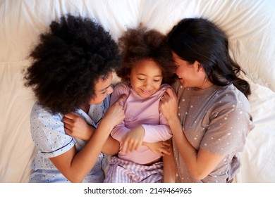 Fotograma De La Familia Con Dos Mamás Con Pajamas Jugando En La Cama De Casa Con Hija Foto de stock
