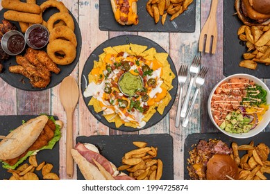Overhead shot of fast food dishes, classic appetizers, tex mex food and in the center a plate of nachos with guacamole on a wooden table