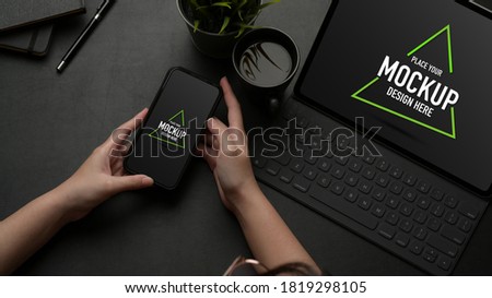Overhead shot of female hands using mock up smartphone on worktable with mock up tablet and coffee cup