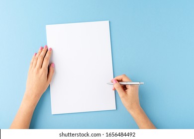 Overhead Shot Of Female Hands Writing With Pen Over Empty White Sheet Of Paper On Blue Background