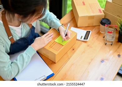 Overhead Shot, Female Online Shop Owner Wiring A Customer Address On A Small Parcel Box At Her Workplace. Small E-commerce Business Concept.