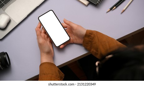 Overhead Shot Of A Female Sits At Her Purple Office Desk And Uses Smartphone. Smartphone White Screen Mockup.