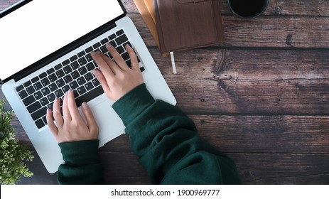 Overhead Shot Of Female Working With Laptop Computer On Wooden Table.