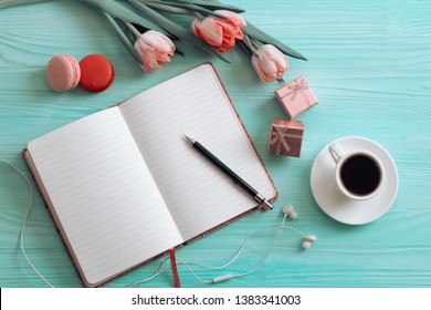Overhead shot of a food journal over empty plates with a cup of coffee and a bouquet of springtime tulip flowers over white wood table top. Flat lay top view style.