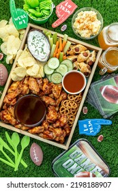 Overhead Shot Of Football Game Day Tailgate Party Food And Snacks With Wings, Wieners, Chips, Dips And Sauces With Football Themed Decorations