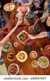 Overhead Shot Of Friends Passing Food Across A Dinner Table