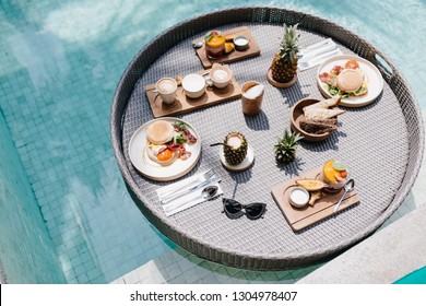 Overhead Shot Of Fruits And Sweets In Pool. Outdoor Photo Of Cup Of Coffee And Pineapple Standing On Table.