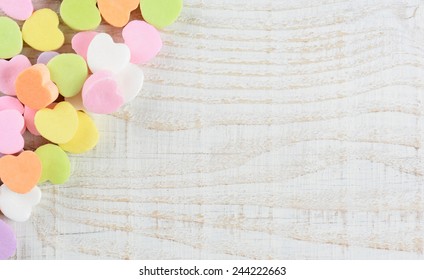 Overhead Shot Of A Group Of Pastel Candy Valentine's Hearts In The Upper Right Corner And Side Of The Frame. Horizontal Format On A Whitewashed Rustic Wooden Table With Copy Space.