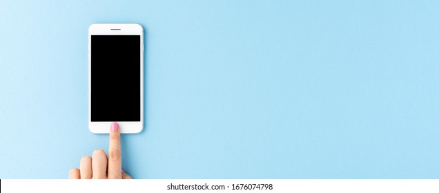 Overhead Shot Of Woman’s Hand Using Smart Phone With Empty Screen On Blue Background. Banner