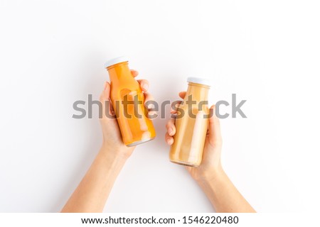 Overhead shot of woman’s hands holding bottles of fruit and vegetable juices isolated on white background