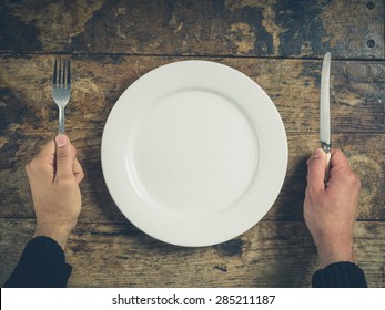 Overhead Shot Of Hands Holding A Knife And Fork By A White Plate On A Wooden Table