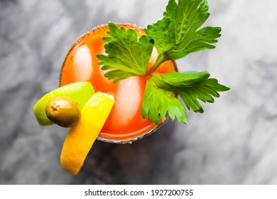 An Overhead Shot Of A Lime, Lemon, Olive, And Parsley Garnished Bloody Mary On A Grey Marble Counter Top.