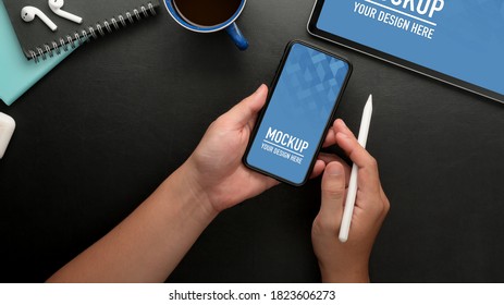 Overhead shot of male using mock up smartphone while holding stylus pen on black table  - Shutterstock ID 1823606273