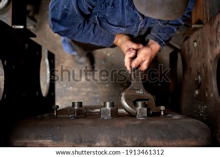 Overhead shot of a man in overalls using a large adjustable spanner to tighten a nut