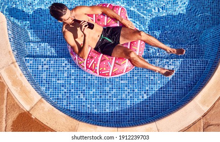 Overhead Shot Of Man In Swim Shorts Floating In Ring Drinking Beer In Outdoor Swimming Pool