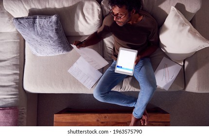 Overhead Shot Of Man Working From Home Sitting On Sofa Reviewing Documents Using Digital Tablet