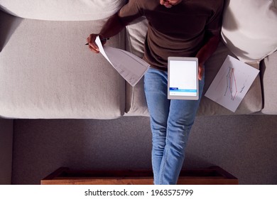 Overhead Shot Of Man Working From Home Sitting On Sofa Reviewing Documents Using Digital Tablet