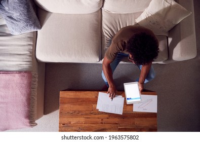 Overhead Shot Of Man Working From Home Sitting On Sofa Reviewing Documents Using Digital Tablet