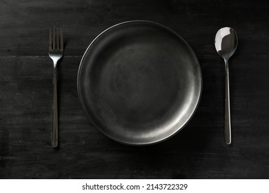 Overhead Shot, Modern Black Dining Table Setting With Empty Black Plate, Fork And Spoon. Flat Lay