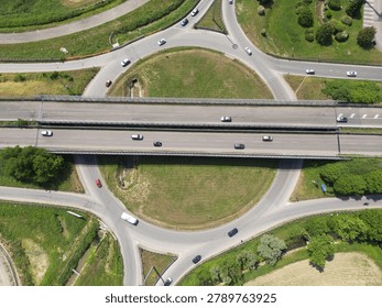 Overhead shot of a multi-lane road intersection surrounded by lush green fields and trees.