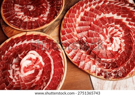 An overhead shot of multiple circular platters filled with premium Iberian cured ham slices for a large event.
