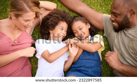 Overhead Shot Of Multi-Racial Family Lying On Grass Tickling Children