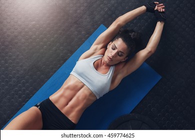 Overhead shot of muscular and fit young woman doing stretching workout exercise mat. Fitness female lying on mat with stretching her hands.