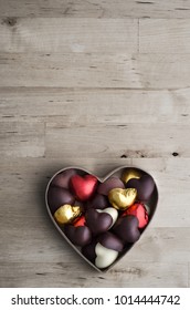 Overhead Shot Of Open Heart Shaped Box Containing A Variety Of Home Made Chocolates On Old, Worn Light Wood Plank Table.