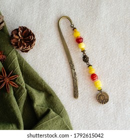 An Overhead Shot Of An Ornate Brass Metal Bookmark With Yellow And Red Pearls On White Fabric