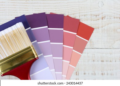 Overhead shot of a paint brush laying on color samples on a rustic white wooden surface. Horizontal format with copy space.